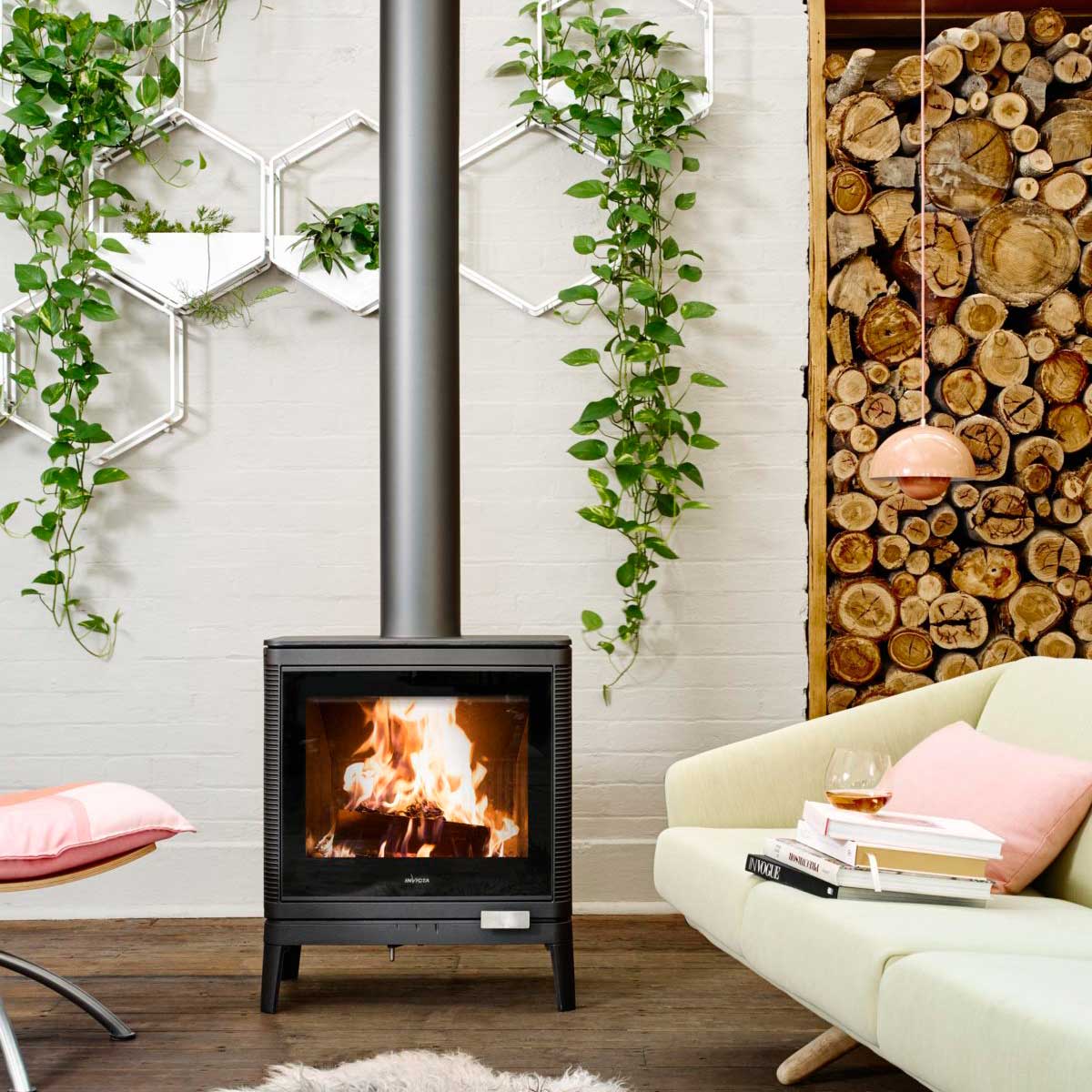 Invicta Kazan wood heater in beautiful interior setting with contemporary white lounge, pink cushions and lush indoor plants