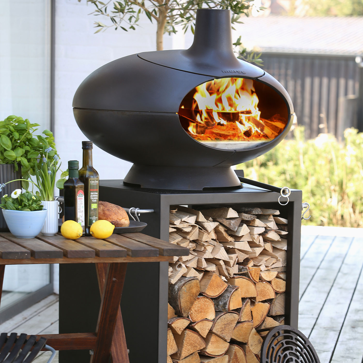 Morso Forno Terra outdoor oven set next to cooking ingredients such as olive oil, lemons and fresh herbs