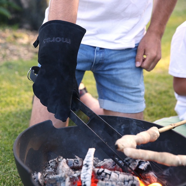 Man with fire glove on using Morso fire tongs over open fire